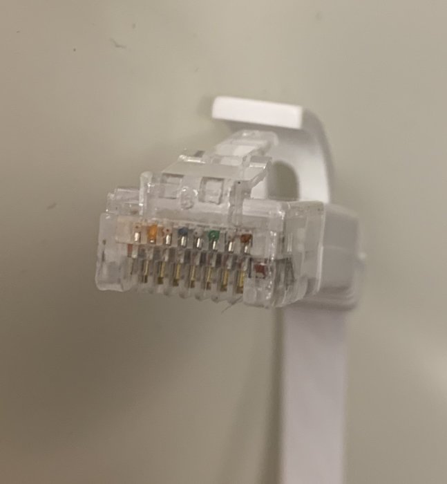 RJ45-kontakt med färgkodade kablar och plastklämma, mot suddig bakgrund.