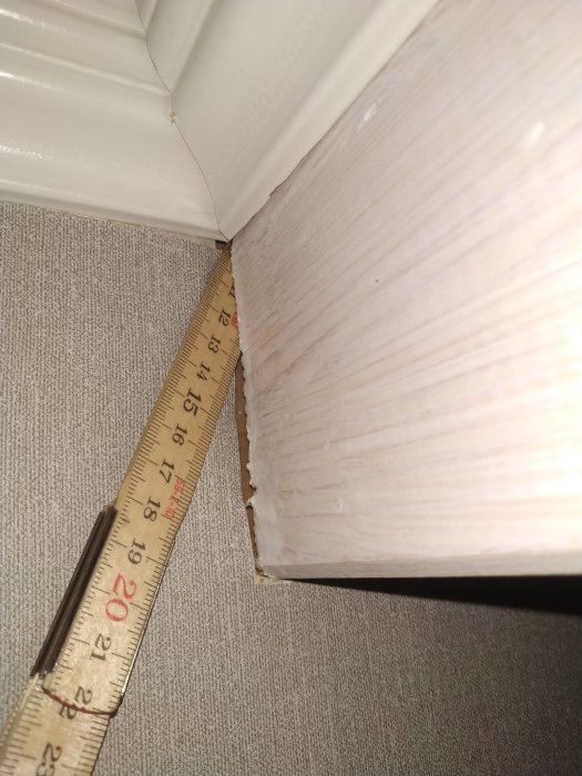 Tumstock som mäter ett 12 cm djupt hål mellan tapetvägg och en balk i taket.