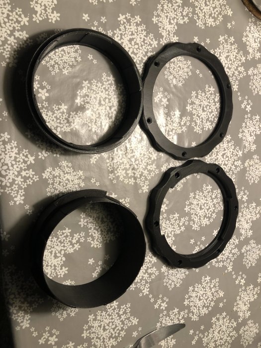 Fyra svarta 3D-utskrivna PLA-delar för koppling till spånsug ligger på ett mönstrat underlag.