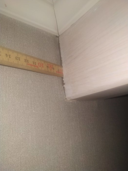 Måttband som mäter hörnet mellan golv och vägg med synlig textur och lister.