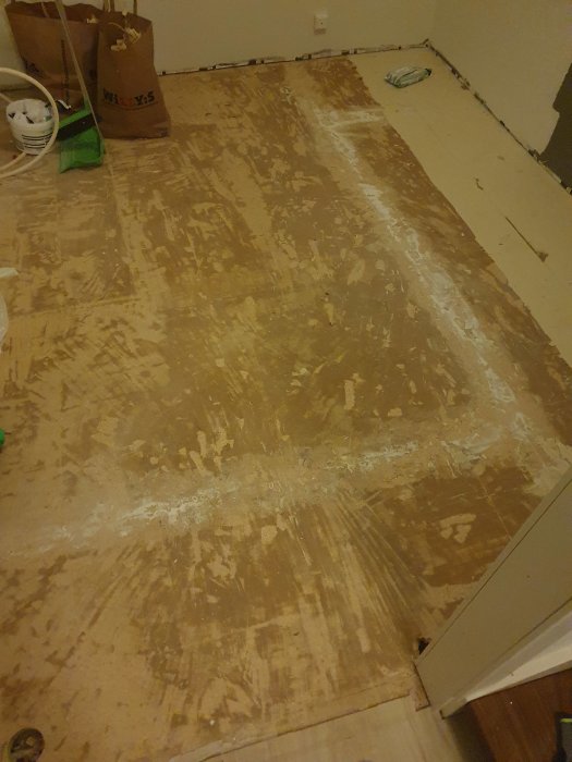 Golvyta med rester av borttaget lim efter att plastmatta avlägsnats i en hall.