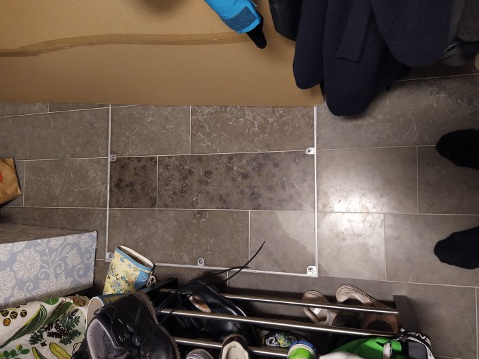 Golv i klädkammare med en integrerad lucka, omgiven av skor och kläder, försedd med skruvar för en vippmekanism.