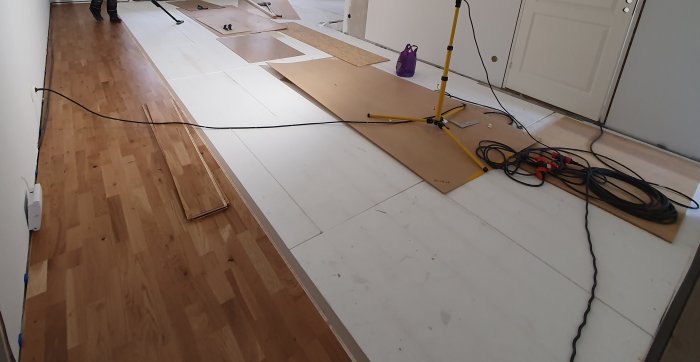 Installation av nytt parkettgolv med masonitskivor på betongunderlag och arbetsverktyg synliga.