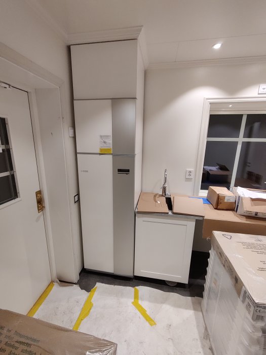 Renoveringsprocess för modern kök med ouppackade skåp och lådor samt gul markering på golv.