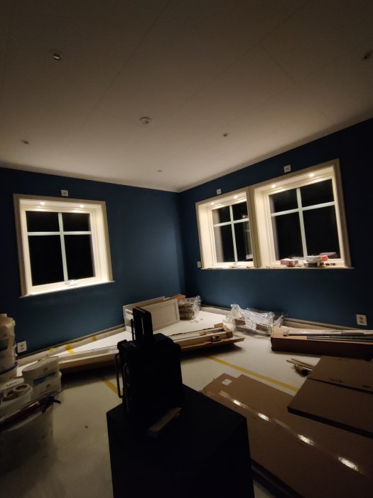 Vardagsrum med blåa väggar under renovering, spotlights i tak och byggmaterial på golvet.