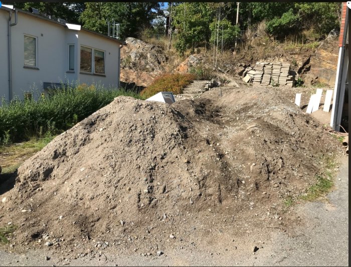 Hög med sandigt grus redo för bortskänkning, lämplig som dränerande fyllnad, på en asfaltväg.