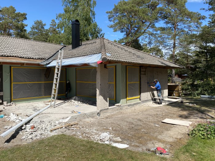 Renovering av husfasad med person som putsar väggen, ommålade garageportar och avlägsnat "pagodtakssväng".