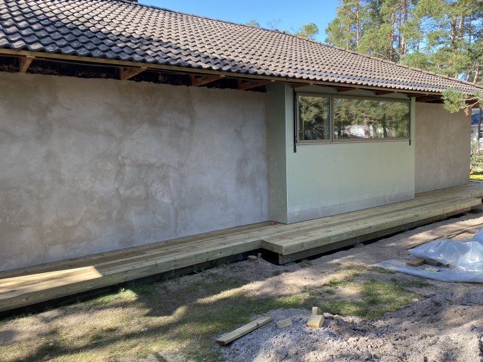 Nybyggd trälandgång längs en putsad vägg på ett hus med ett halvfärdigt burspråk.