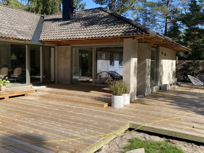 Trädäck i trädgården nästan färdigställt vid ett hus, med några brädor och detaljer som ska slutföras.
