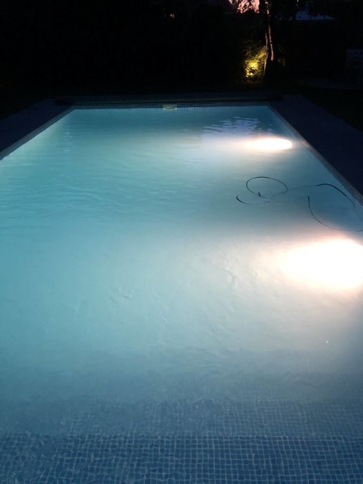 Upplyst pool vid skymning med kabel på ytan men ingen synlig poolrobot.