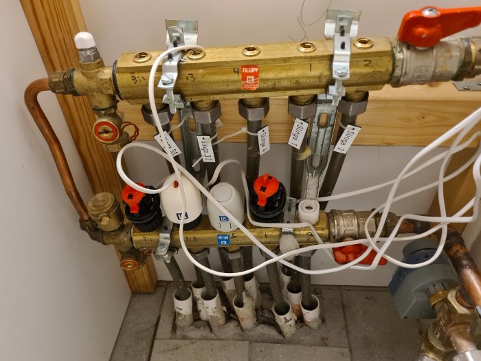 Bild av golvvärmesystem med flera kopplade rör och ventiler, etiketter märker olika slingor.