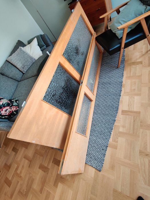 Gammal dubbeldörr med glasrutor liggande på ett trägolv i ett hemmiljö, tänkt för återinstallation.