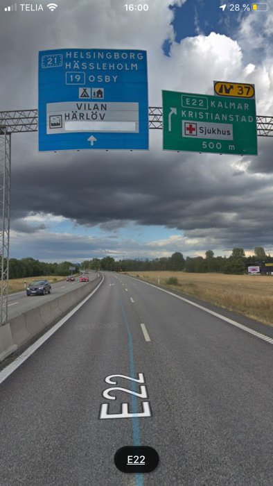 Trafikskyltar som visar vägval för E22 mot Kristianstad och avfart för Helsingborg med mörkt molnigt himmel i bakgrunden.