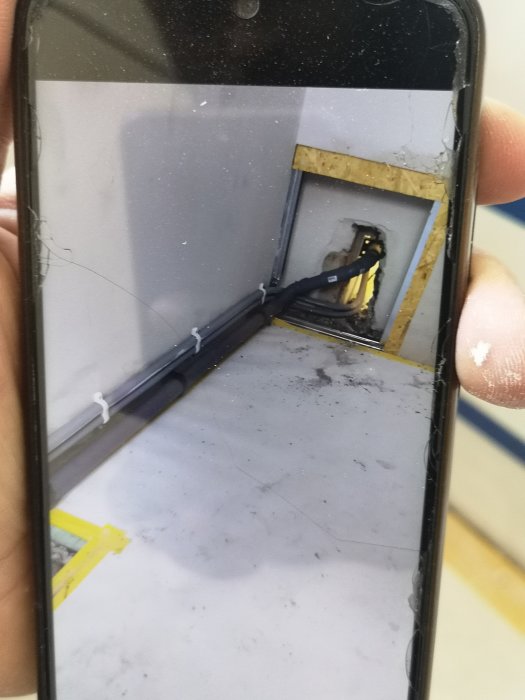 Nya VVS-rör längs golv och in i inspektionslucka, syns genom smutsig telefon.