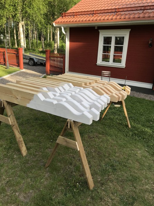 Närbild av hemgjorda taktassar i trä, placerade på arbetsbockar utomhus framför rött hus med tegeltak.