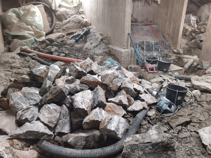 Byggarbetsplats med sprängda stenar, verktyg och en bergborr, indikation på pågående arbete.