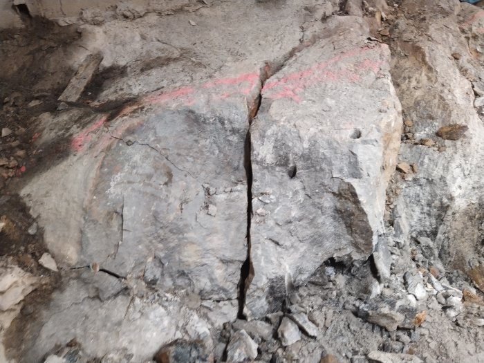 Stor sten med sprickor och röd markering för bergspräckning under ett pågående byggprojekt.