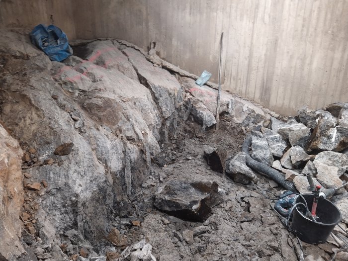 Stort berg i en grävd grop markerat för spräckning bredvid sprängsten och verktyg.