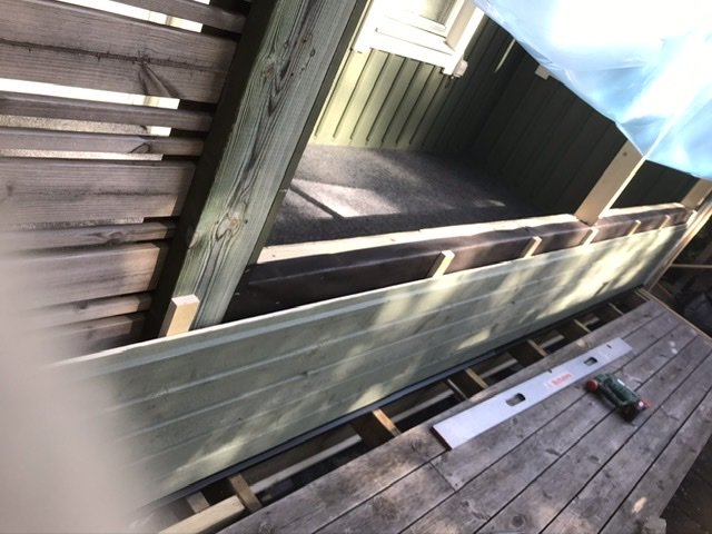 Installationsprocess för ett fönsterbleck bakom träpanel mot golvregel med synliga verktyg.