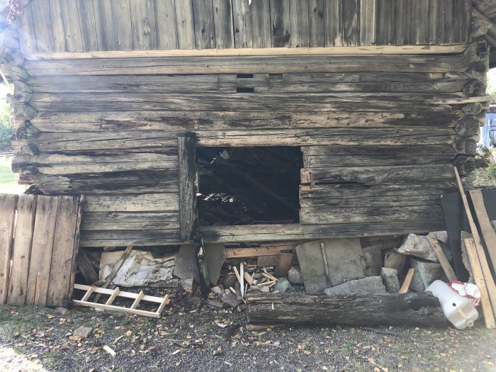 Förfallen lada med bråte och en ofullständig stengrund vilar på lösa stenar vid en kortsida.