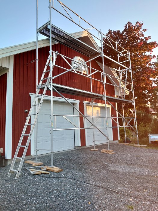 Ställning uppställd utanför ett rött garage med vita dörrar redo för målning.