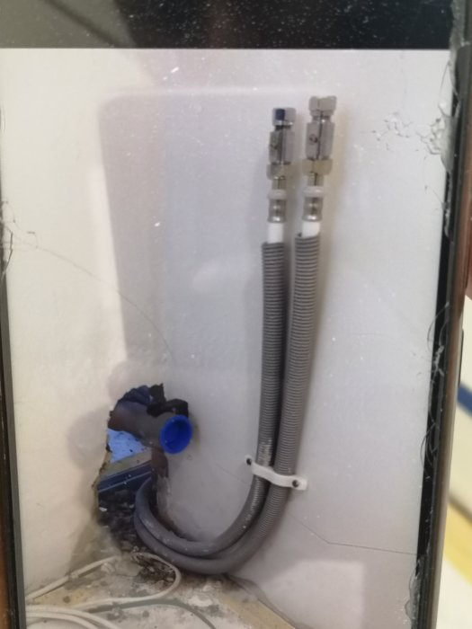 Avloppsrör och flexibla vattenledningar i en öppen vägg utan avstängningsventiler.