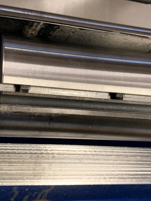 Närbild på en räfflad stålinmatningsvals med synliga avstånd och märken, indikerande slitage eller justeringsbehov.