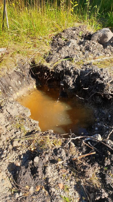 Testgrop på blivande byggtomt fylld med vatten, visande jordlager av sand och lera.