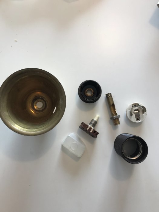 Isärplockade delar av en golvlampa, inklusive lamphållare, tryckbrytare och metallstolpe.