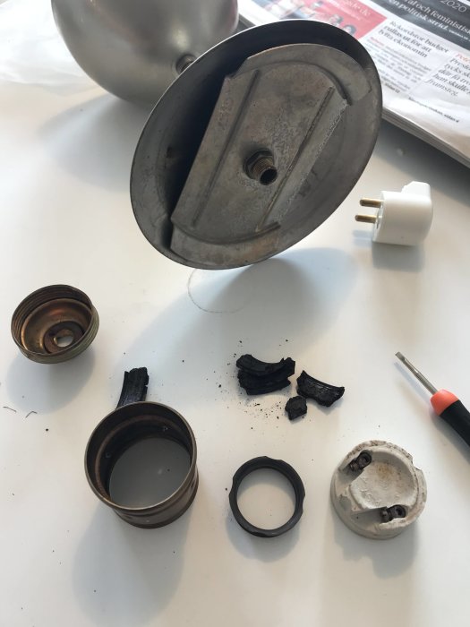 Isärplockade delar av en lampa med en torr, smulig plastdel, en obruten sladd, och andra komponenter på ett bord.