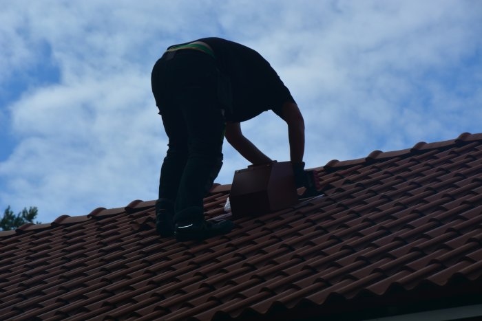 Person som installerar rör genom tak på ett rött tegelhus för ventilationssystemet.