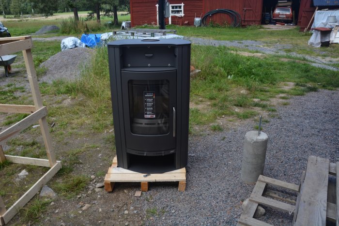 Svart vattenmantlad kamin "Caron Aqua" placerad utomhus på en pall, redo för installation.