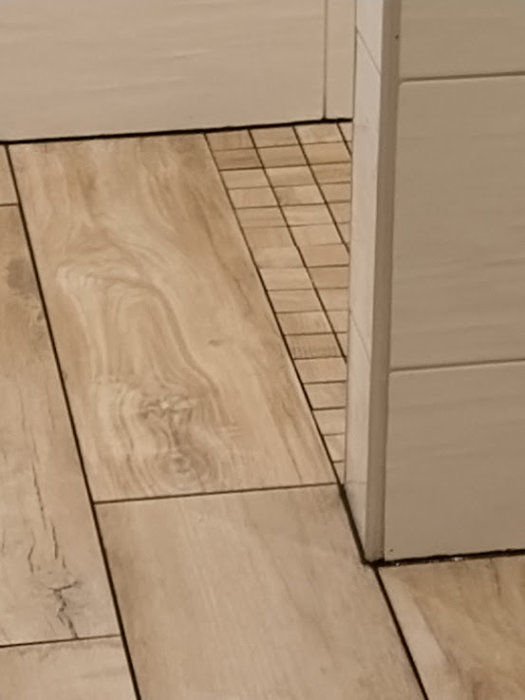 Renoverat badrumsgolv med träimitationsklinker och ojämn mosaik nära golvbrunnen.