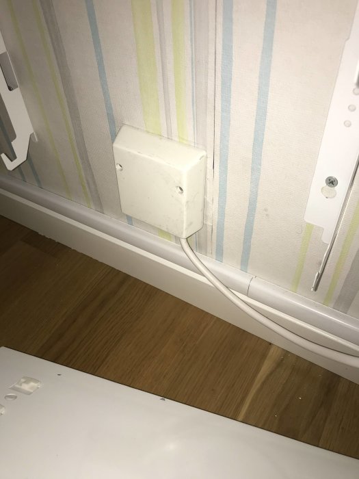 Vit elbox på vägg med lister och tapet, kabel dragen nedåt mot golvet.