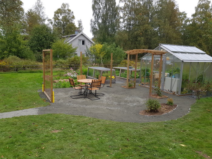 Nygrusad uteplats med trädgårdsmöbler, pergola och växthus i en trädgård.