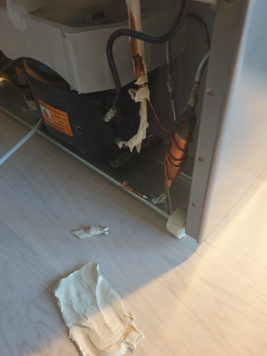Smält och avlossat plastskydd vid en Electrolux frys kompressor och ledningar.