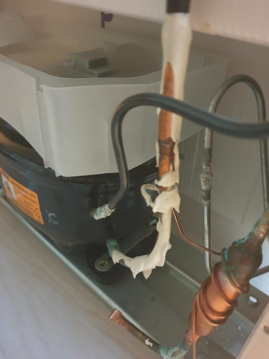 Smält och skadat plastskydd bakom en Electrolux frys med synlig korrosion på rör.