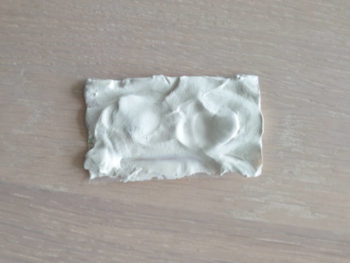 Smält och deformerat plastskydd på trämönstrat underlag, troligen från hushållsapparat.