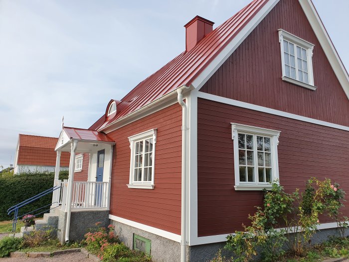 Rödmålat trähus med farstukvist, vita fönsterknektar och fodrade fönster.