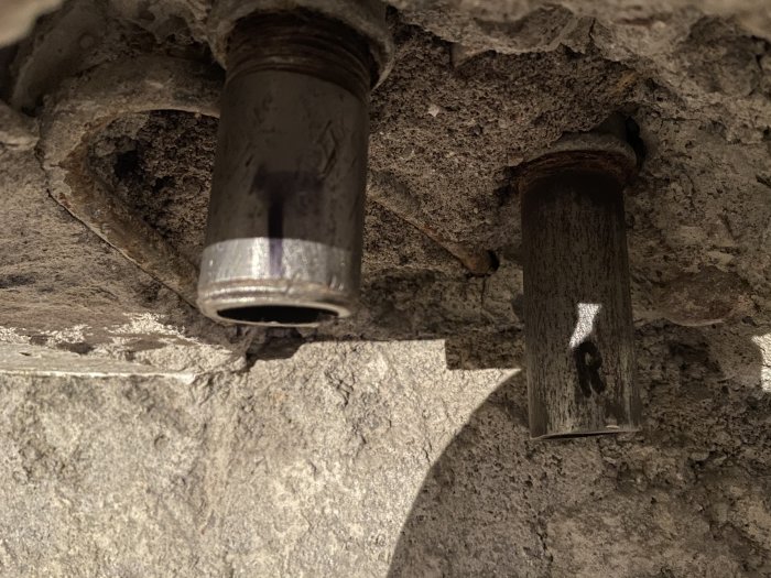 Kapade stålrör sticker ut från betongvägg, delvis genomskuret och slitna ytor syns.