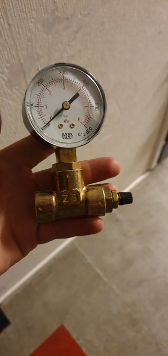 Tryckmätare med manometer kopplad till ett T-kors i mässing hållen i handen.