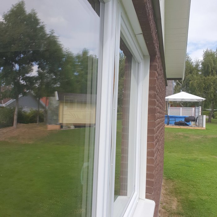 Nytt fönster på hus med reflektion av trädgård, ifrågasatt kvalitet och montering av bleck.