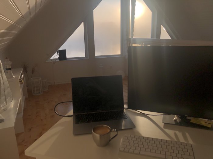 Uppdaterad hemarbetsplats med dator, skärm, tangentbord och kaffekopp på skrivbordet, ljust rum.