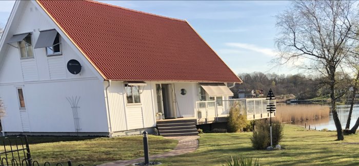 Utomhustrappa vid vit husfasad med röd tak, med utsikt över sjö och natur.