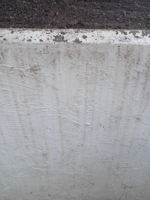 En delvis målad vit stödmur i cement med nötningsmärken och gulaktiga missfärgningar.