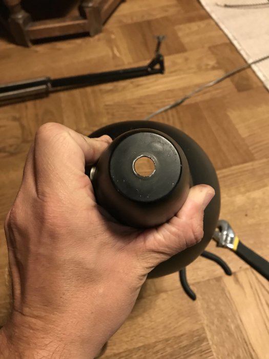 Hand håller en renoverad skrivbordslampa med ny svart lampsladd och inaktiv tryckknapp på toppen.