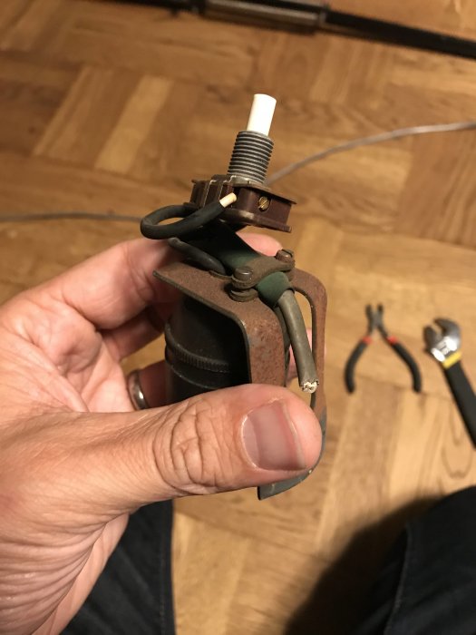 Person som håller i en trasig lamphållare och gammal lampsladd under renovering.