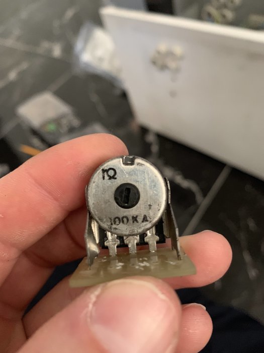 Hand håller en elektrisk säkring med märkningen 100kA på en otydlig konstruktionsbakgrund.