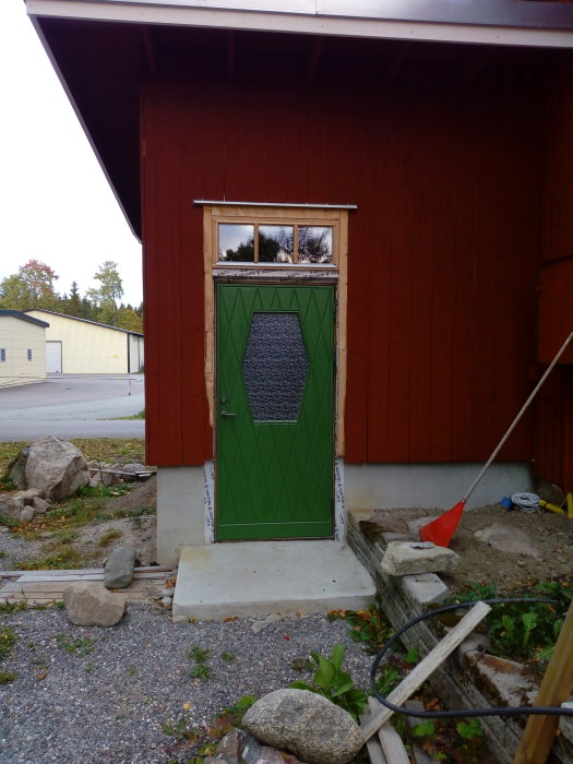 Nyinstallerad kromoxidgrön ytterdörr på en röd trävägg, med byggmaterial framför på en villa under renovering.