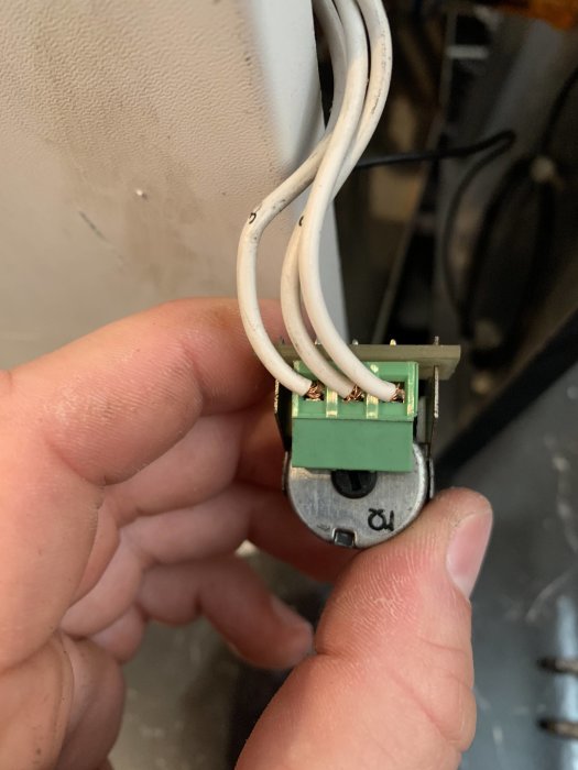 En hand håller en öppen eluttag med synliga anslutna ledningar och installeringar.